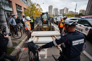 Police and protesters stand by as workers begin to remove the bike lanes along Bloor Street West in Toronto on Wednesday, Oct. 14, 2026. THE CANADIAN PRESS/Arlyn McAdorey